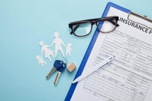 family insurance paperwork with house keys, pens and glasses